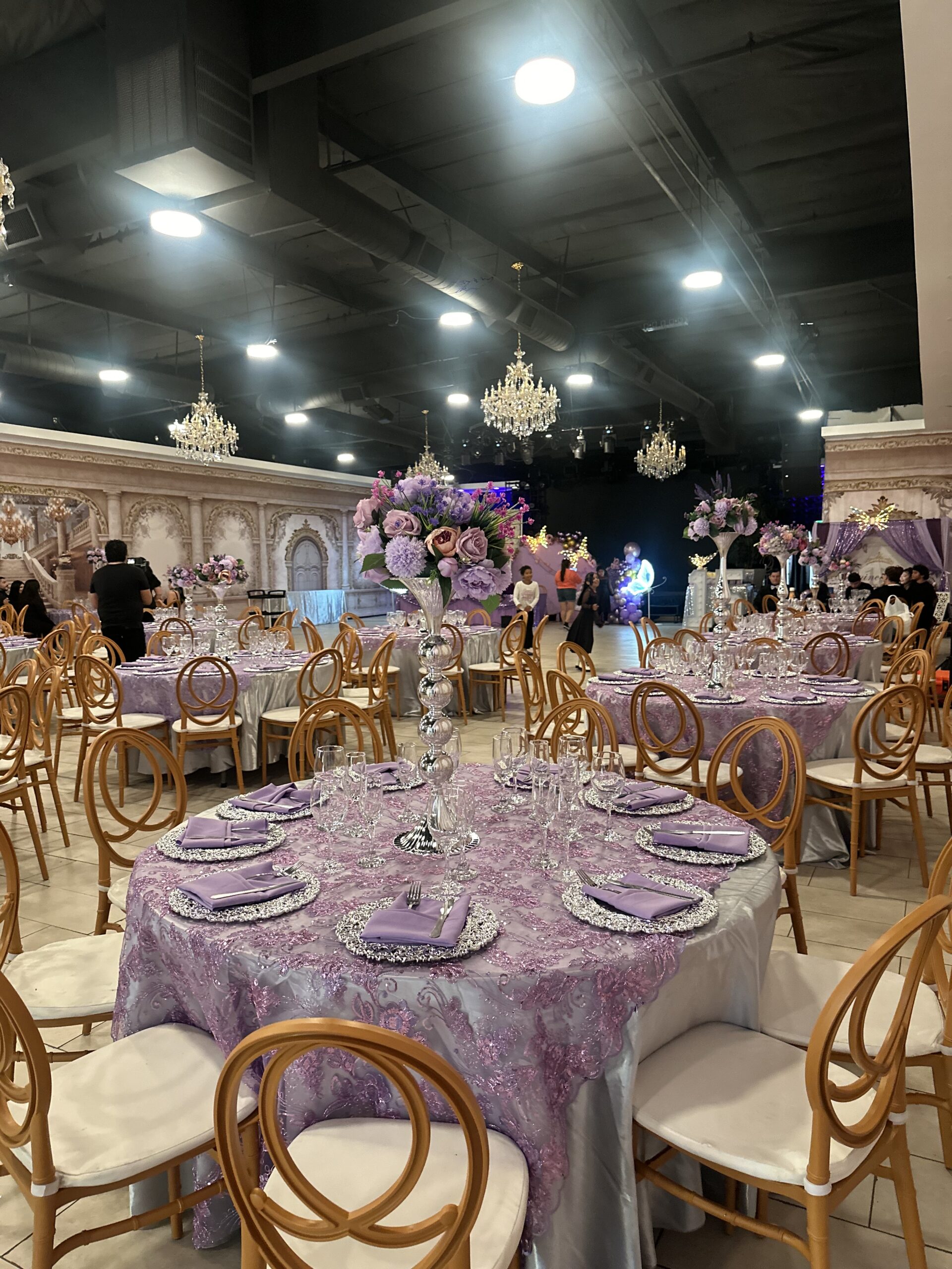 Lavender lace tablecloths with silver chargers and purple floral centerpieces at Lavender Venue