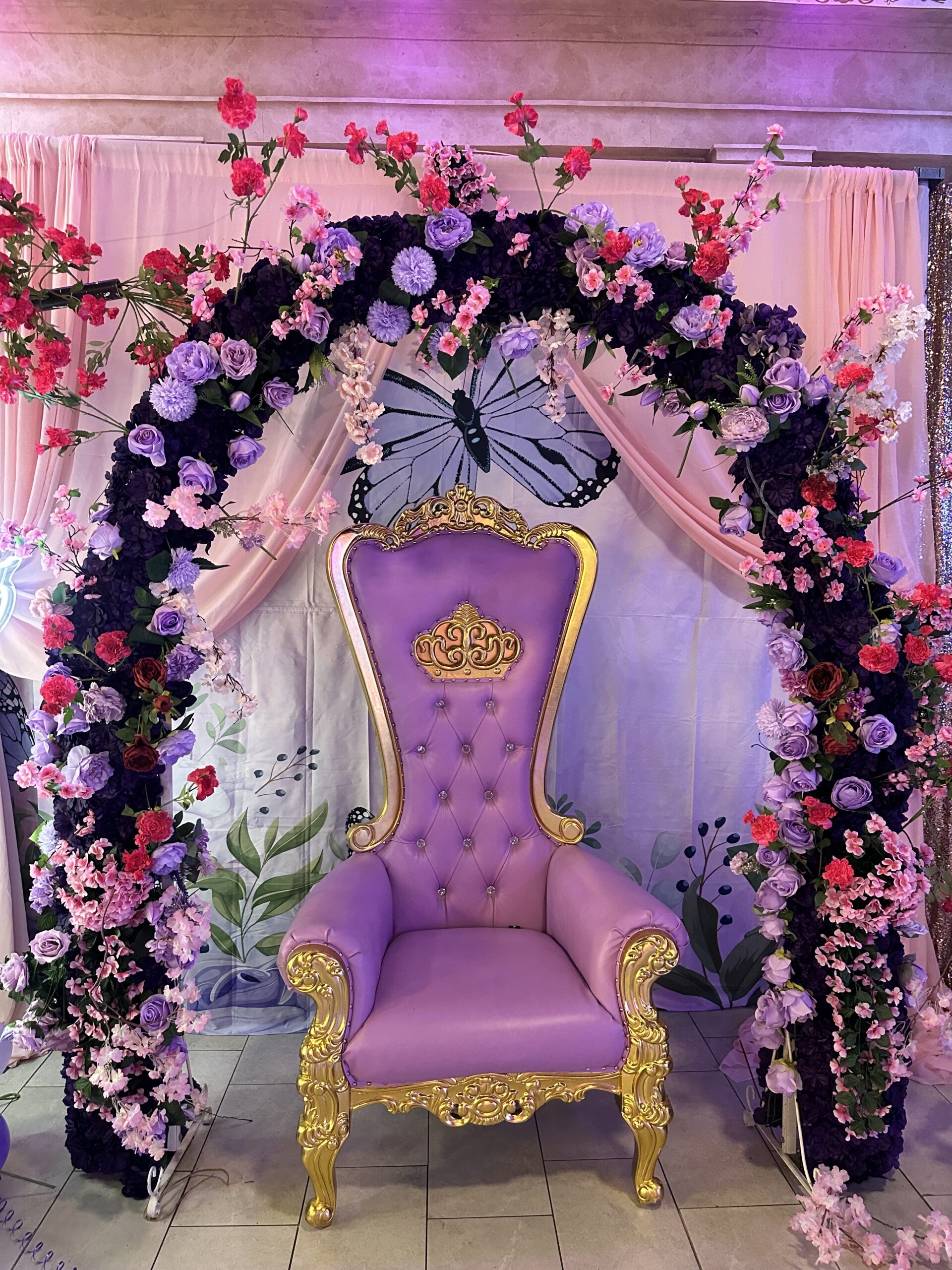 Purple throne chair with floral arch and butterfly decorations for quinceañera at Lavender Venue